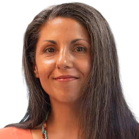 Smiling woman with long gray hair wearing a coral top and beaded necklace.