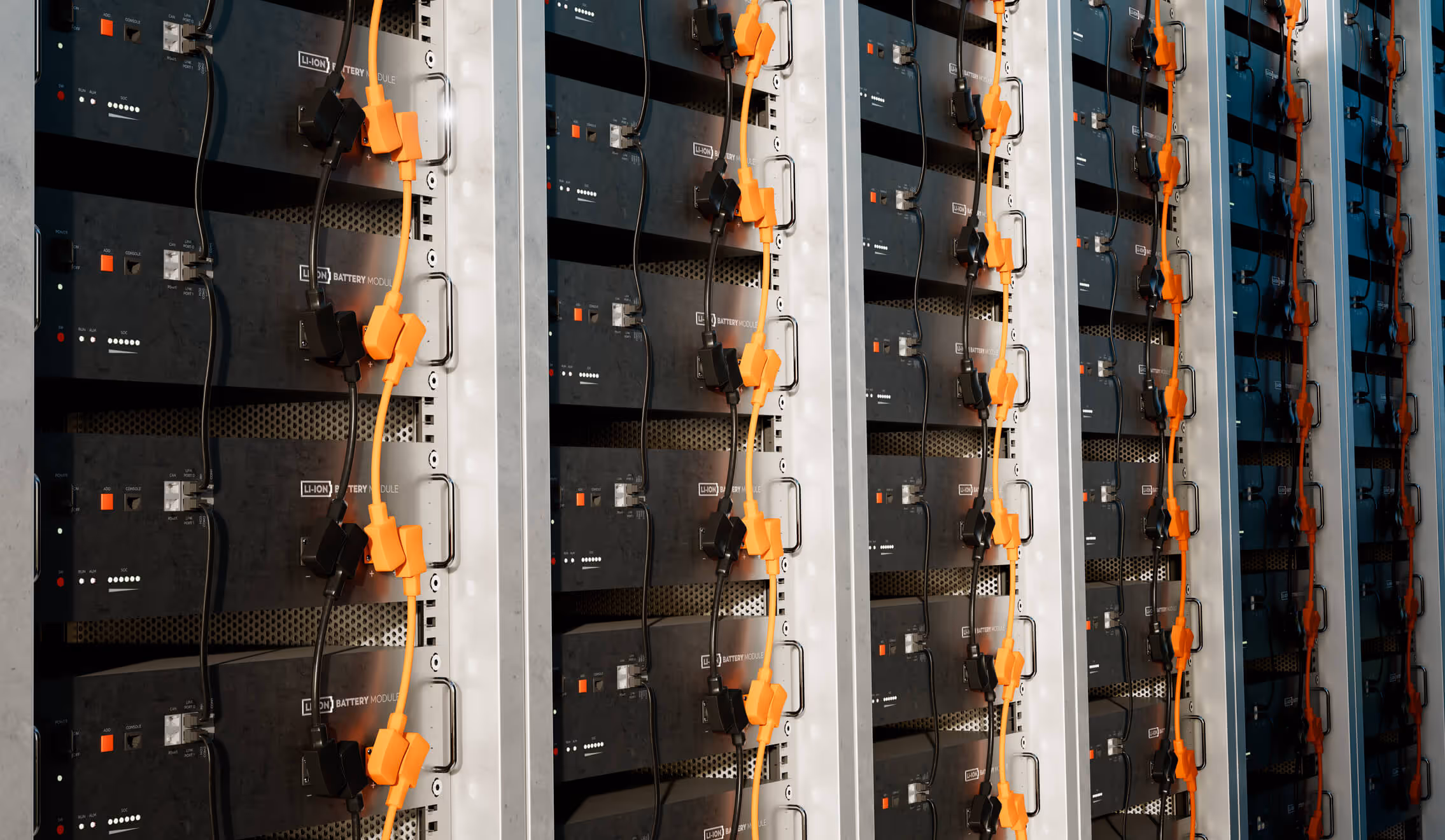 Rows of black lithium-ion battery modules with orange and black cables connected, mounted in industrial metal racks.