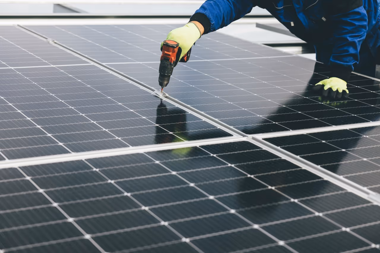 Person wearing gloves using a drill to install solar panels on a rooftop.